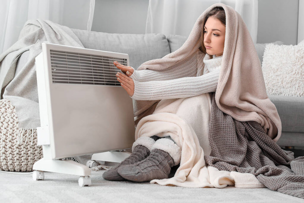 Jeune femme en plaids se réchauffant les mains près du radiateur à la maison - Photo, image