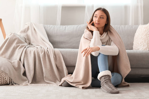 Junge Frau mit warmem Karo sitzt zu Hause auf dem Fußboden - Foto, Bild