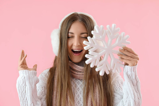 Happy young woman in warm ear muffs with big snowflake on pink background - Photo, Image
