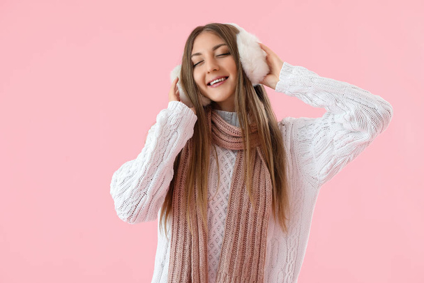Young woman in warm ear muffs and scarf on pink background - Photo, Image