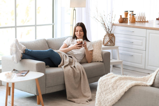 Young woman with glass cup of cocoa lying on grey sofa in kitchen - Foto, immagini