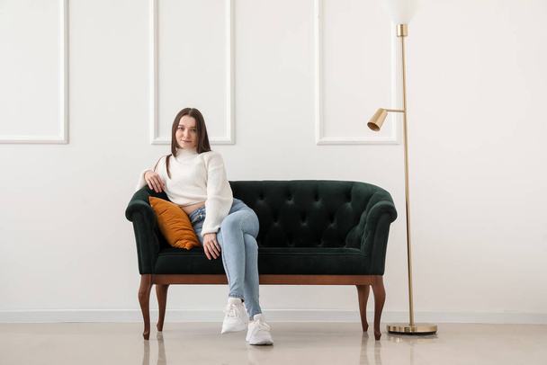 Junge Frau sitzt auf grünem Sofa nahe Lichtwand - Foto, Bild