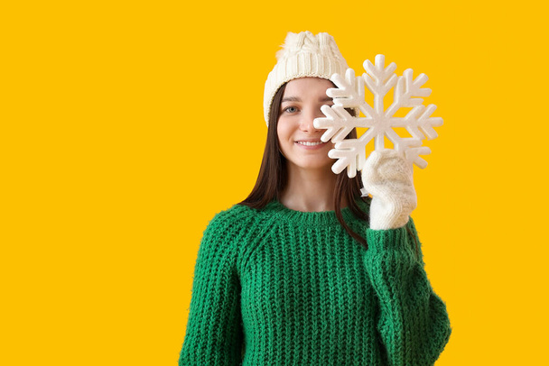若いです女性で暖かいです帽子で大きな雪の結晶で黄色の背景 - 写真・画像
