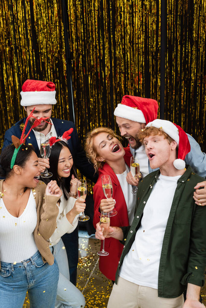 High angle view of excited multiethnic business people with champagne dancing near tinsel in office  - Foto, imagen