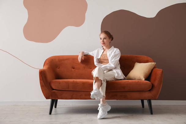 Красива жінка сидить на червоному дивані біля кольорової стіни
 - Фото, зображення