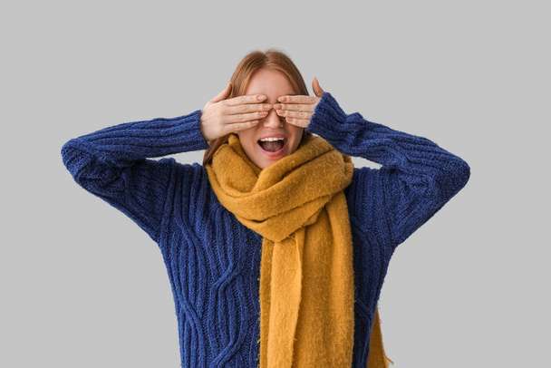 Молодая рыжая женщина в теплом шарфе закрывает глаза на сером фоне - Фото, изображение