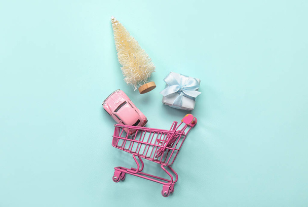 Shopping cart with Christmas tree, toy car and gift on blue background - Photo, Image