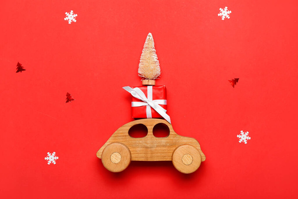 Игрушечный автомобиль с елкой и подарок на красном фоне - Фото, изображение