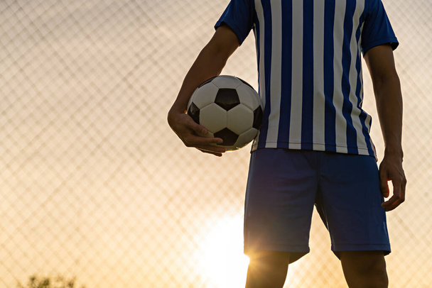 Athlete standing with ball on football field during sunrise, soccer ball in net on sky background, ball movement, popular sports on football club. - Photo, Image