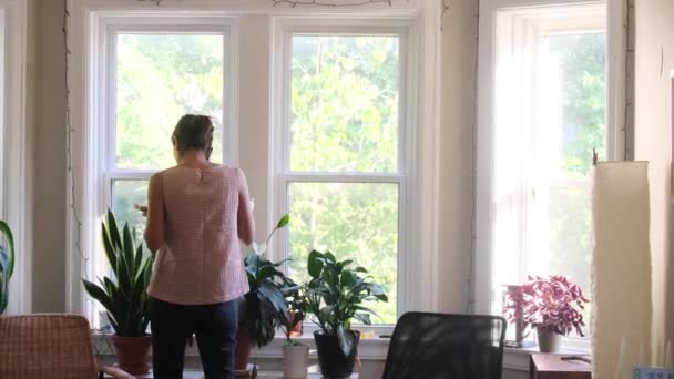 imagens da visão traseira da jovem mulher com smartphone na frente da janela em casa - Filmagem, Vídeo