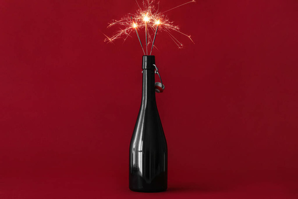 Champagne bottle with burning Christmas sparklers on color background - Фото, зображення