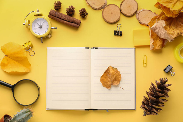 Komposition mit leerem Notizbuch, Schreibwaren, Wecker und Herbstblättern auf gelbem Hintergrund - Foto, Bild