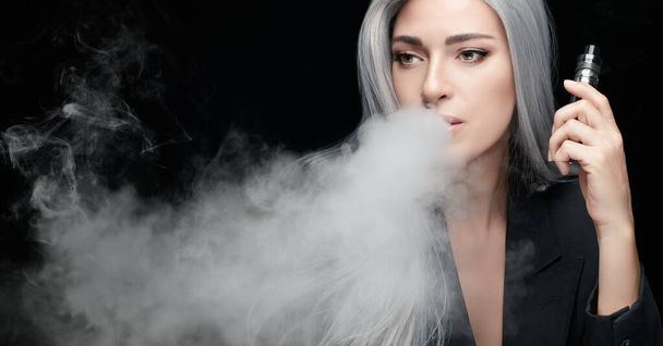 Smoking girl with a vaping device. Silver haired woman blowing a big smoke cloud. Panorama banner isolated on black background with copy space - Foto, Imagen