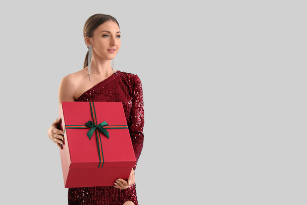 Young woman in red dress with Christmas gift on grey background - Fotó, kép