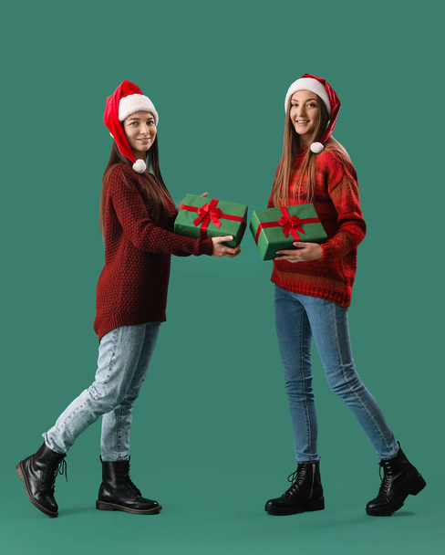 Young women in Santa hats with Christmas gifts on green background - Foto, afbeelding