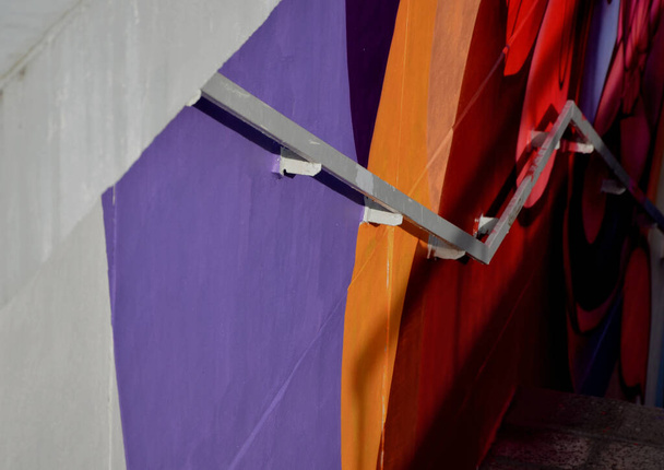 μεταλλική λαβή σκυροδέματος πλευρά της σκάλας με τοίχους συγκράτησης διατρέχει έδαφος της κλίσης. υπόγεια σήραγγα κάτω από δρόμο πολλαπλών λωρίδων. πολύχρωμοι πίνακες φτιάξει ζοφερό τσιμέντο σήραγγες - Φωτογραφία, εικόνα
