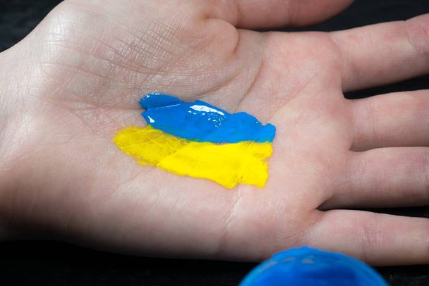 Meisje tekent de vlag van Oekraïne op haar hand. Ondersteuning van het Oekraïense volk. Stop de oorlog tegen Oekraïne. Stop de Russische invasie.. - Foto, afbeelding