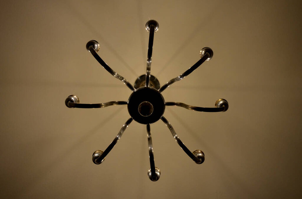 old historical eight-armed chandelier. silver single with spruce cone shaped bulbs and a ball at the bottom. white room with curtain. bottom view. candlestick shape, spider - Photo, Image