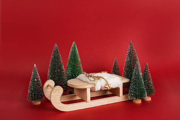 екологічні Натуральні дерев'яні іграшкові санки з ялинками на червоному тлі. Новорічний подіум для ваших продуктів
 - Фото, зображення