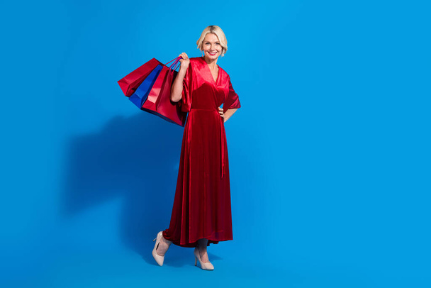 Full length photo of funny sweet retired lady dressed shiny red outfit holding bargains empty space isolated blue color background. - Fotoğraf, Görsel