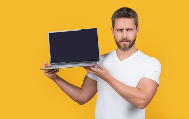 man showing app on laptop. man showing app on screen with copy space. man showing app isolated on yellow studio background. man showing laptop app in studio. - Photo, Image