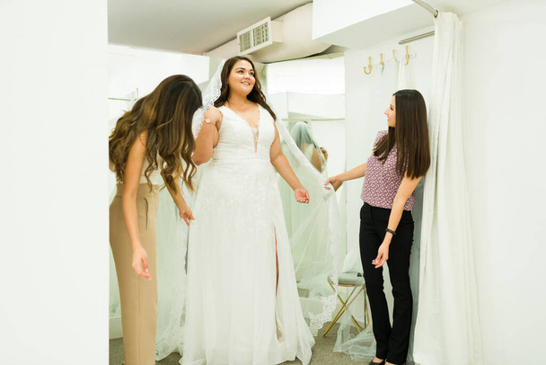 Латиноамериканская пухленькая женщина покупает свадебное платье со своими подружками и подружками в свадебном магазине - Фото, изображение