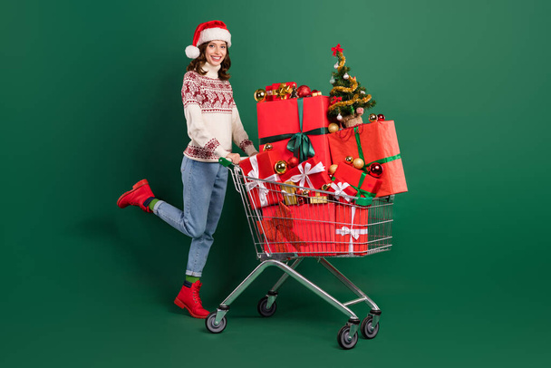 Full size photo of positive pretty girl push market trolley pile stack newyear giftbox isolated on green color background. - Foto, Bild
