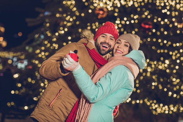 Photo of two funny excited people hold arms dancing have fun enjoy x-mas evening tree lights outdoors. - Foto, Imagen