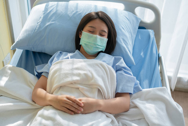 Triste mujer asiática paciente acostada en la cama del hospital y con una máscara facial para proteger el coronavirus. Concepto de atención médica, coronavirus de cuarentena (COVID-19) y seguro de salud. - Foto, Imagen