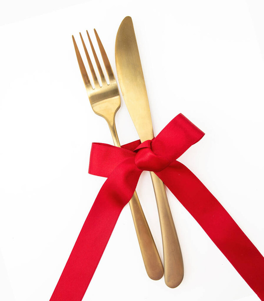 Ünnepi asztal beállítása felülnézet. Arany villa, kés és piros szatén szalag dekoráció elszigetelt fehér. Karácsony, Valentin napi ünnepi vacsora - Fotó, kép