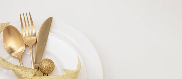 Рождественский стол, закрывающий вид. Золотые столовые приборы и украшения на белых блюдах, копировальное пространство, вид сверху. Элегантность и роскошь - Фото, изображение