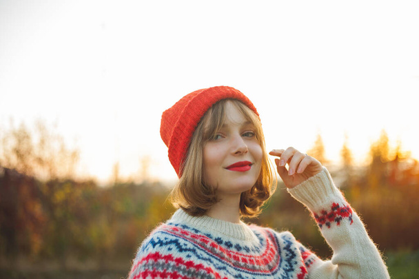 Φωτεινό πορτρέτο χειμώνα μιας όμορφης νεαρής γυναίκας σε ένα πλεκτό κόκκινο καπέλο στο φόντο των χριστουγεννιάτικων δέντρων. Οικολογικά Χριστούγεννα, χειμερινές διακοπές. - Φωτογραφία, εικόνα