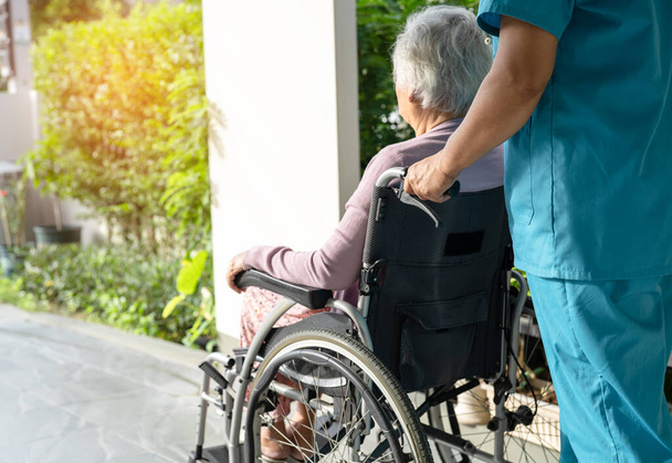 Φροντιστής βοήθεια και φροντίδα ασιατική ανώτερος ή ηλικιωμένη ηλικιωμένη γυναίκα ασθενή κάθεται σε αναπηρική καρέκλα στη ράμπα στο νοσηλευτικό νοσοκομείο, υγιή ισχυρή ιατρική έννοια - Φωτογραφία, εικόνα