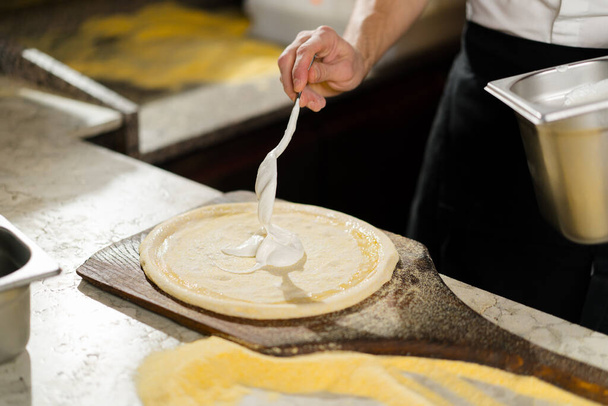 No restaurante, um chef profissional prepara pizza, adiciona molho à massa. Cozinhar comida orgânica deliciosa. Movimento lento - Foto, Imagem