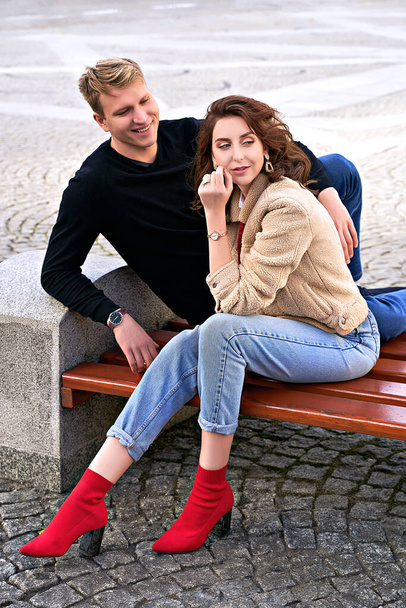 Beautiful young couple sitting on a bench in the city during a romantic date. Urban lifestyle. - Zdjęcie, obraz