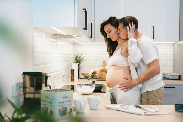 Pregnancy photo session at home, in the kitchen, in the room on the bed, by the window and in the bathroom, brushing your teeth, putting your hands on your tummy and making cheesecakes from flour - Photo, image