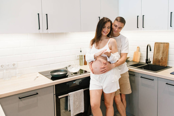Pregnancy photo session at home, in the kitchen, in the room on the bed, by the window and in the bathroom, brushing your teeth, putting your hands on your tummy and making cheesecakes from flour - Photo, Image