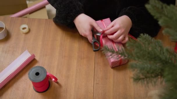 Mujer envolviendo un regalo en papel despojado con cinta roja. Manos empacando una caja en el papel de navidad rojo y blanco.  - Metraje, vídeo