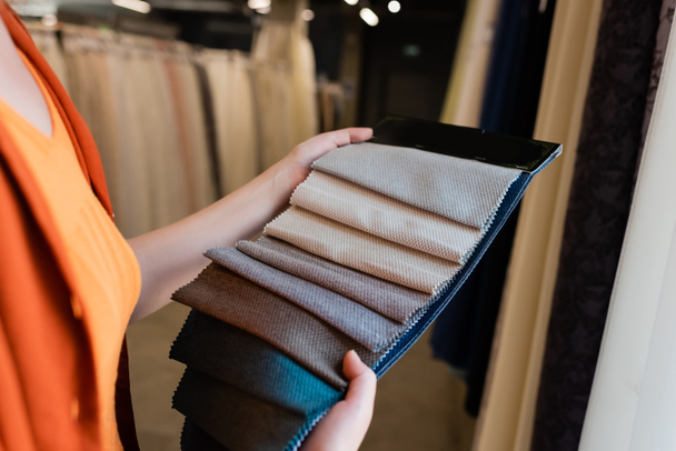Vue recadrée d'un client flou tenant des échantillons de tissu dans un magasin de textiles  - Photo, image