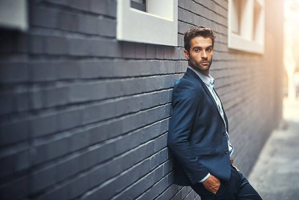 Fashion, suit and city with a business man or model leaning against a brick wall outdoor for contemporary style. Corporate, executive and trendy with an edgy male posing in the alley of an urban town. - Photo, Image