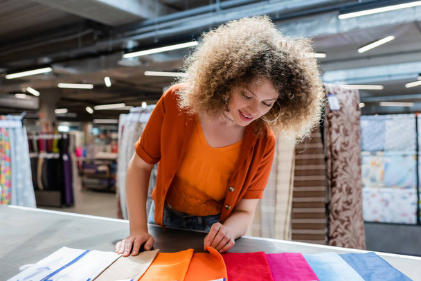 Позитивний покупець вибирає тканину з різнокольорових зразків на столі в текстильному магазині
  - Фото, зображення