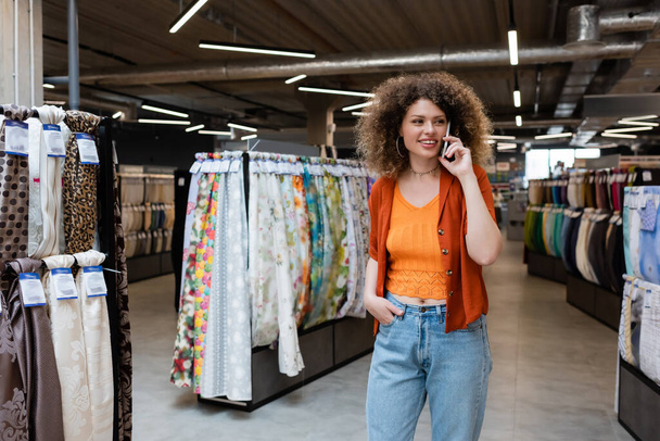 Кучерявий клієнт розмовляє на мобільному телефоні біля зразків тканини в текстильному магазині
  - Фото, зображення
