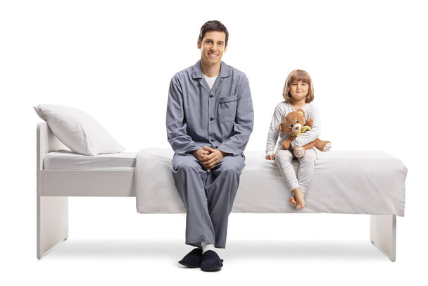 Father and daughter in pajamas sitting on a bed isolated on white background - Fotoğraf, Görsel