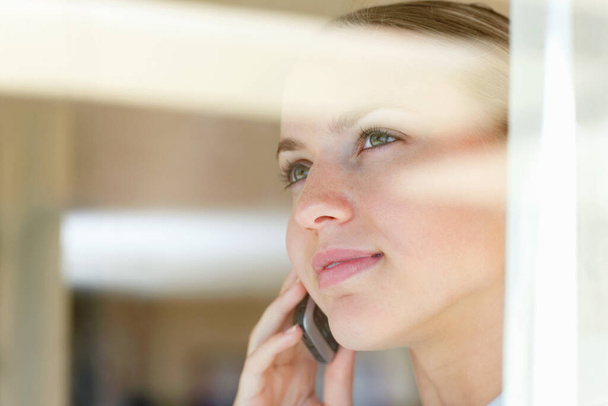 Женщина говорит по телефону, смотрит через стекло. Молодая женщина разговаривает по телефону, смотрит через стекло - Фото, изображение