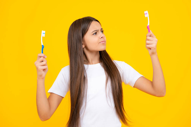 Girl cleans her teeth with a brush. Portrait beautiful teen holding toothbrush brushing teeth isolated on yellow background, Dental health concept. Angry face, upset emotions of teenager girl - Photo, image