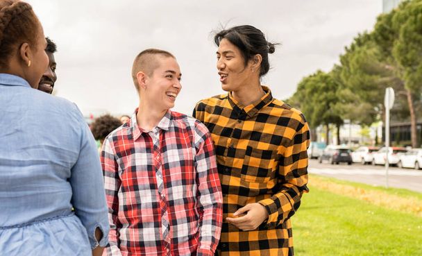 Δύο νέοι άνθρωποι μη δυαδικού φύλου απολαμβάνουν με άλλους φίλους σε ένα δημόσιο πάρκο. - Φωτογραφία, εικόνα