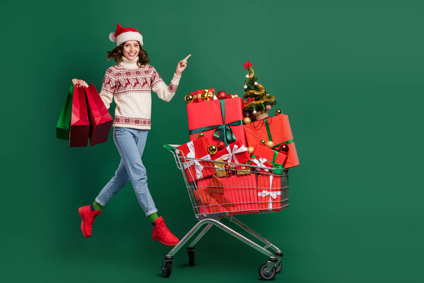 Full body portrait of beautiful lady jump hold bags direct finger empty space pile stack box package trolley isolated on green background. - Foto, Imagem