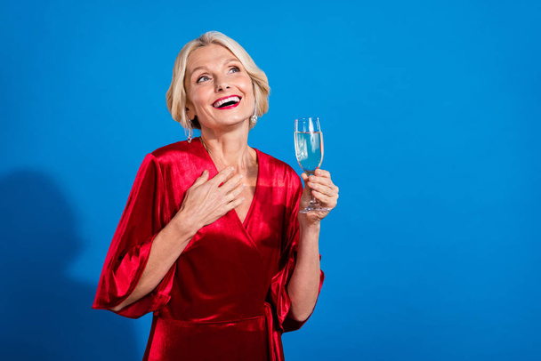 Photo of pretty excited retired lady dressed shiny red outfit enjoying wine looking empty space isolated blue color background. - Foto, Imagen