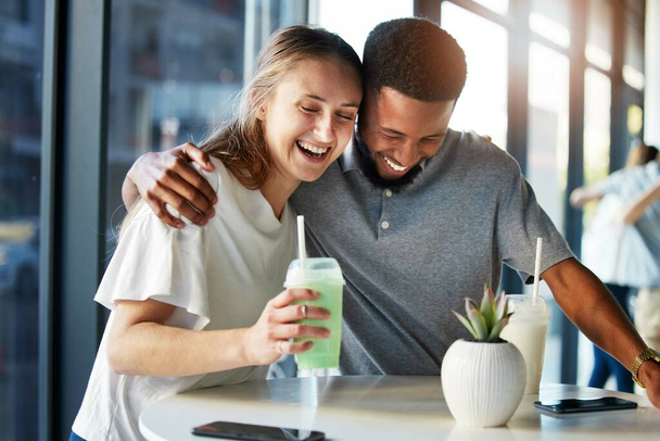 Dating, restaurant and couple with smoothie drink hugging, having fun and laughing together on romantic date. Love, relationship and interracial couple enjoying milkshake, cocktail and juice in cafe. - Photo, Image