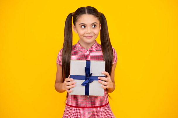 Happy teenager, positive and smiling emotions of child girl. Teenager kid with present box on isolated yellow background. Teen girl giving birthday gift. Present, greeting and gifting concept - Photo, Image